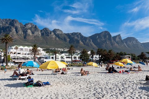 People relaxing on Camps Bay Beach with the Twelve Apostles mountains in the background

